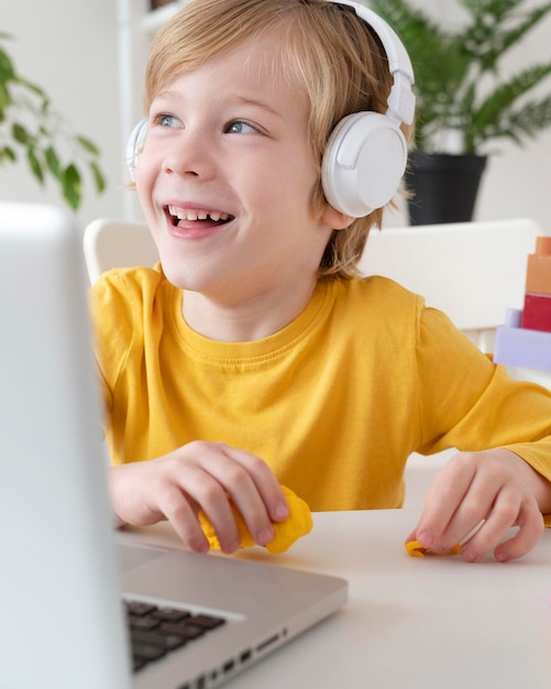 Niño sonriente con ordenador portátil y auriculares en casa