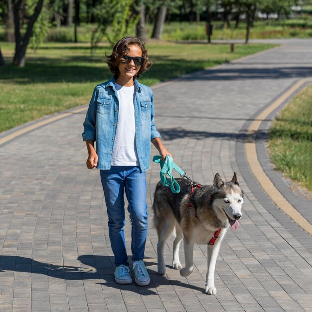 Niño sonriente en el parque paseando al perro