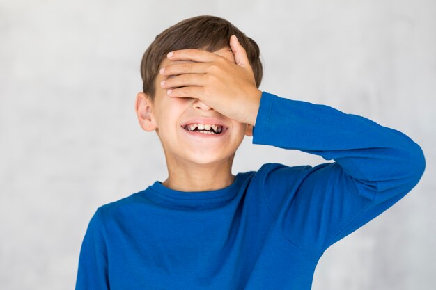 Niño sonriente que cubre sus ojos