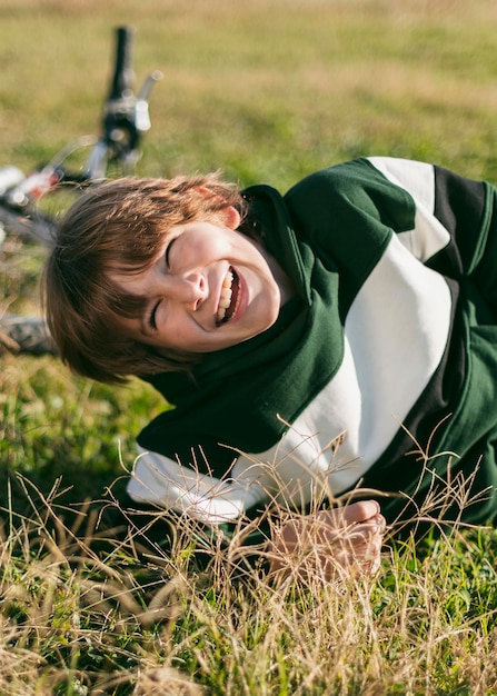 Niño sonriente relajándose sobre el césped mientras monta su bicicleta