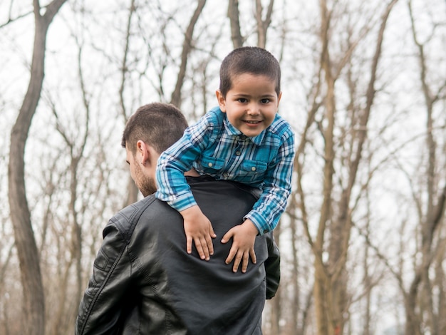 Niño sonriente retenido por su padre al aire libre