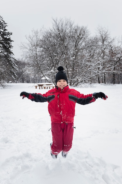 Niño sonriente saltando en tierra nevada en temporada de invierno