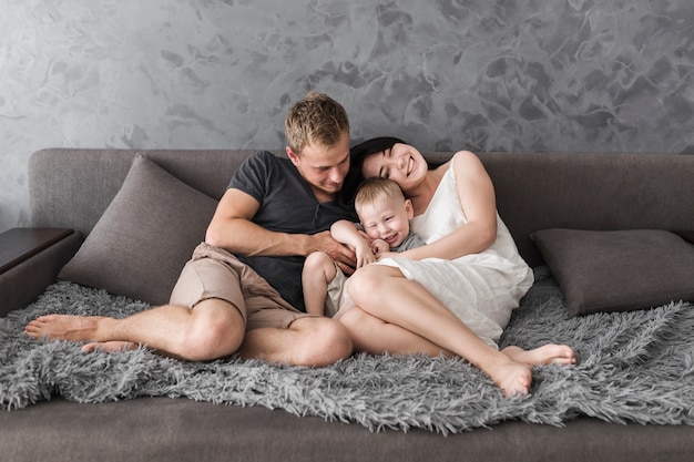 Niño sonriente sentado entre sus padres en el acogedor sofá gris