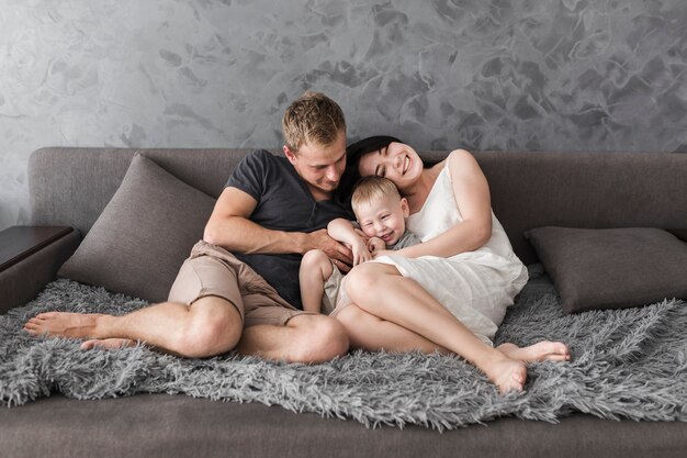 Niño sonriente sentado entre sus padres en el acogedor sofá gris