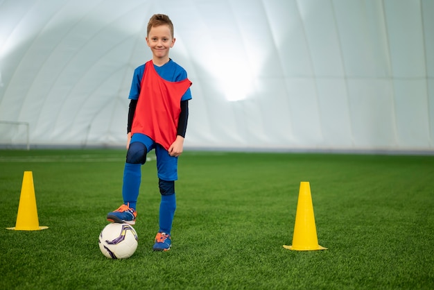 Niño sonriente de tiro completo en el campo de fútbol