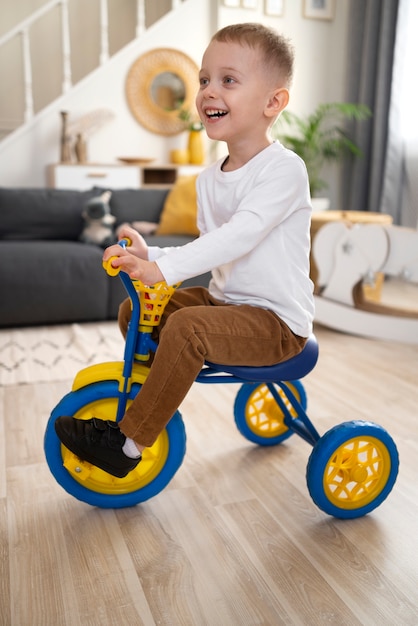 Niño sonriente de tiro completo montando triciclo en casa