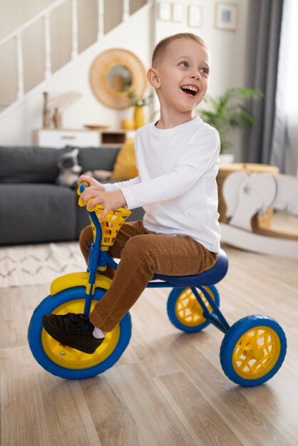 Niño sonriente de tiro completo montando triciclo en el interior