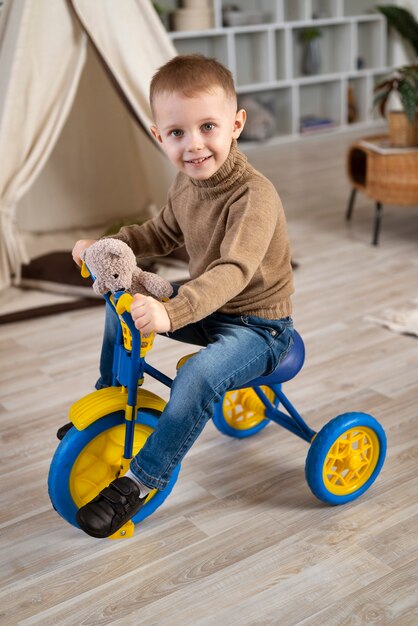 Niño sonriente de tiro completo sentado en triciclo