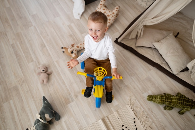 Niño sonriente de tiro completo con triciclo en casa
