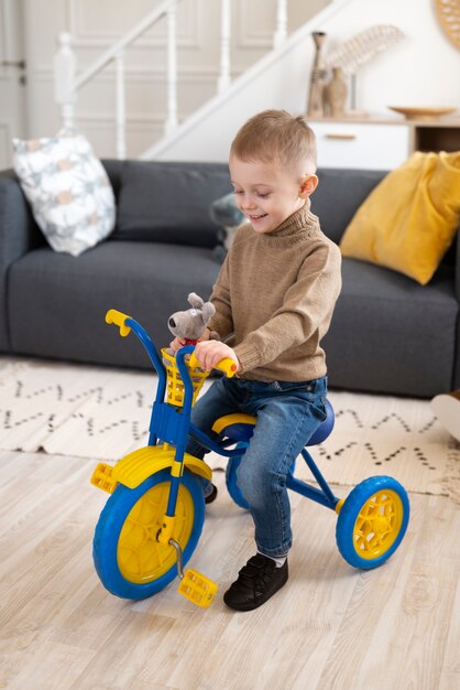 Niño sonriente con triciclo en el interior tiro completo