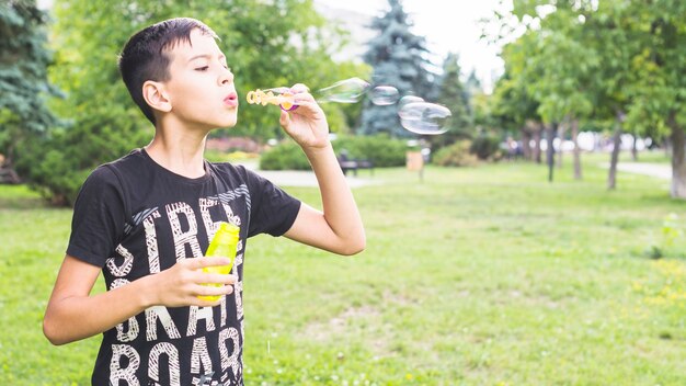 Niño soplando burbujas con la varita de burbujas en el jardín