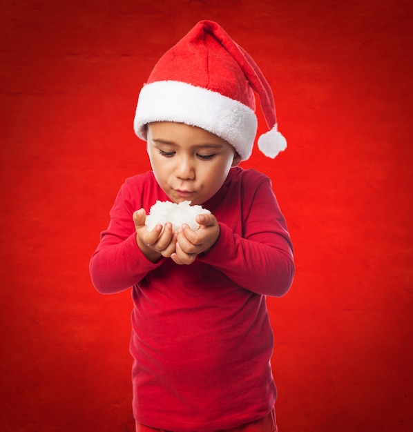 Foto gratuita niño soplando a la nieve en un fondo rojo