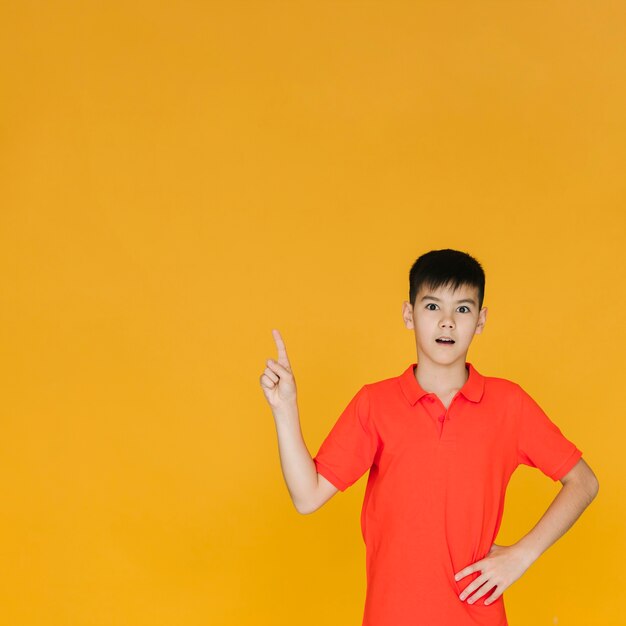 Niño sorprendido apuntando hacia arriba con copia espacio