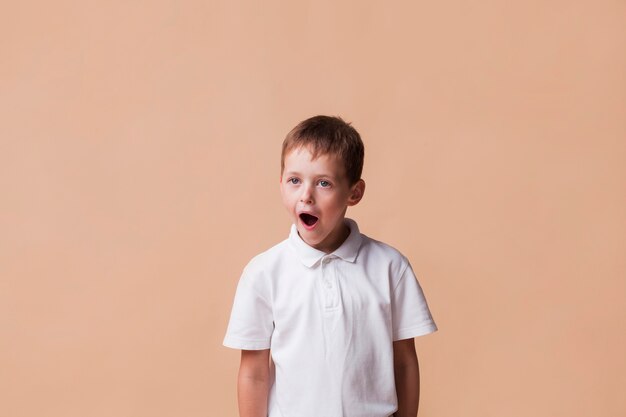 Niño sorprendido con la boca abierta de pie cerca de fondo beige