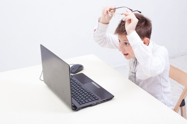 El niño sorprendido usando su computadora portátil sobre fondo blanco.