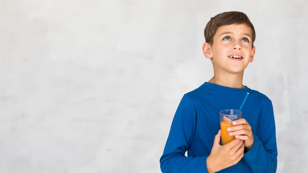 Foto gratuita niño sosteniendo un jugo de naranja y mirando hacia arriba