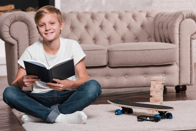 Niño sosteniendo un libro y sentado cerca de un sofá