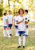 Foto gratuita niño sosteniendo una pelota de fútbol afuera junto a otros niños