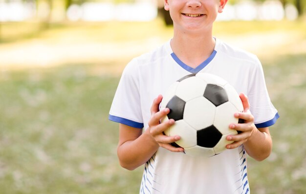 Niño sosteniendo una pelota de fútbol al aire libre con espacio de copia