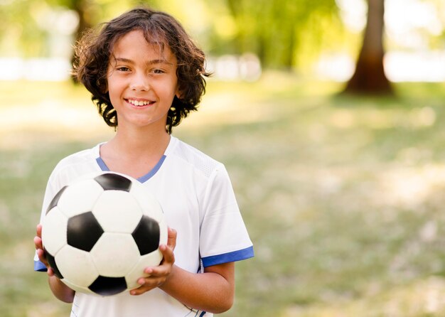 Niño sosteniendo una pelota de fútbol con espacio de copia