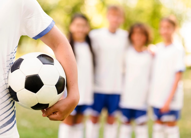 Niño sosteniendo una pelota de fútbol junto a sus compañeros de equipo desenfocado