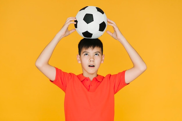 Niño sosteniendo una pelota de fútbol en su cabeza