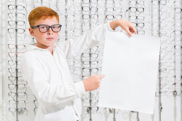 Foto gratuita niño sosteniendo y señalando papel blanco negro en tienda de óptica