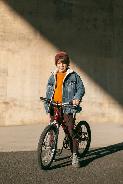Niño con su bicicleta afuera en la ciudad.