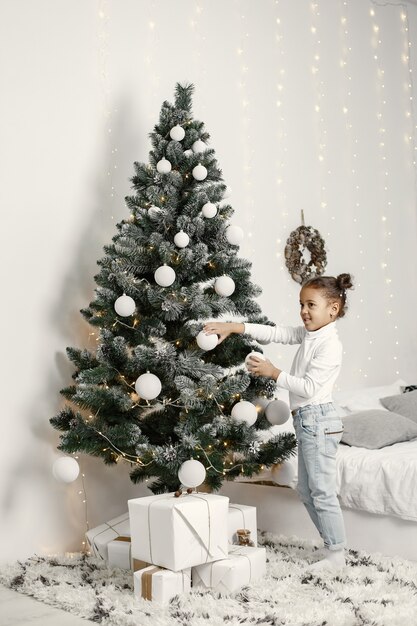 Niño con un suéter blanco. Hija de pie cerca del árbol de Navidad.