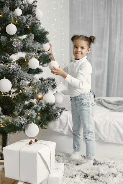 Niño con un suéter blanco. Hija de pie cerca del árbol de Navidad.