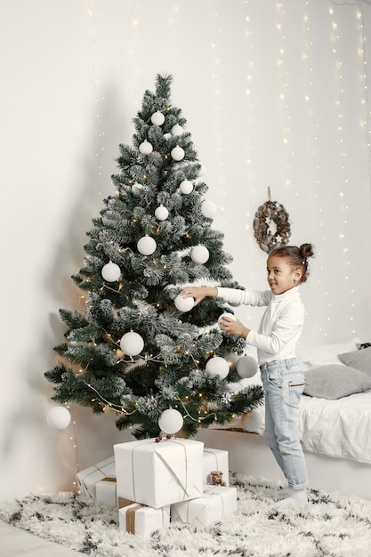 Niño con un suéter blanco. Hija de pie cerca del árbol de Navidad.