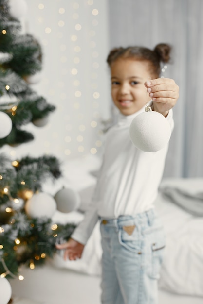 Niño con un suéter blanco. Hija de pie cerca del árbol de Navidad.