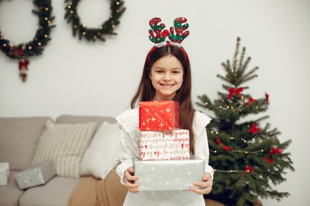 Niño con un suéter blanco. Hija sentada cerca del árbol de Navidad.