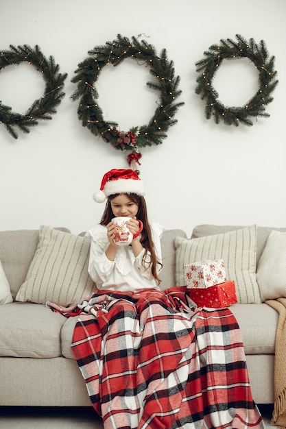 Niño con un suéter blanco. Hija sentada cerca del árbol de Navidad.