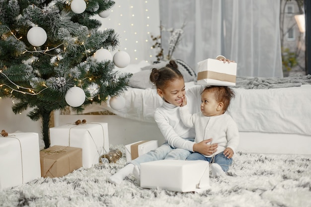 Niño con un suéter blanco. Hijas stitting cerca del árbol de Navidad. Dos hermanas en casa.