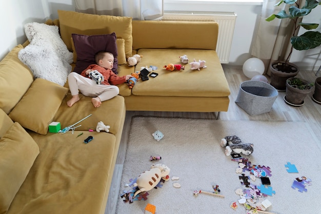Niño de tiro completo acostado en el sofá con juguetes