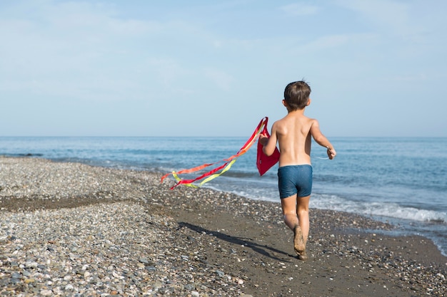 Foto gratuita niño de tiro completo jugando con cometa en la playa