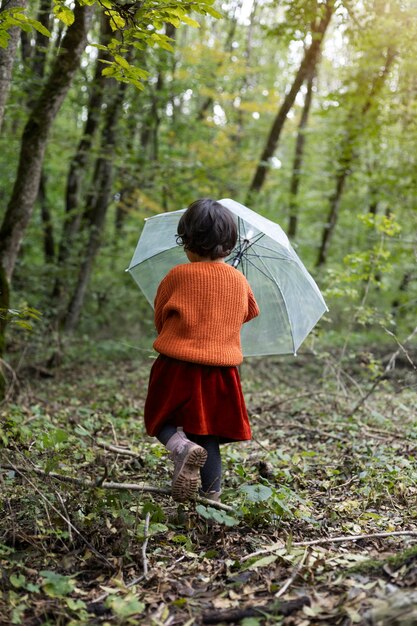 Niño de tiro completo en la naturaleza con paraguas