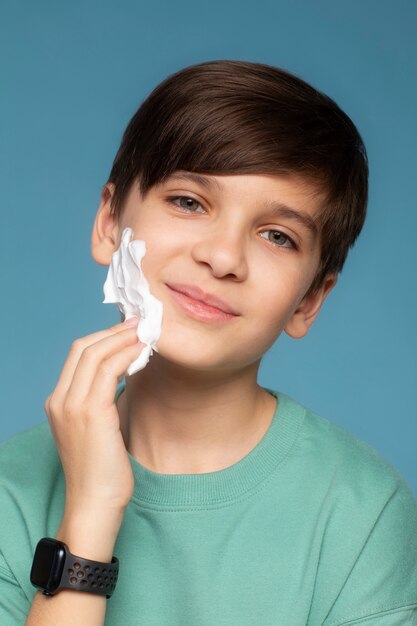 Niño de tiro medio aplicando crema de afeitar.