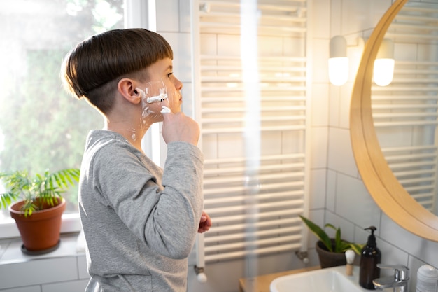 Niño de tiro medio aprendiendo a afeitarse en el espejo