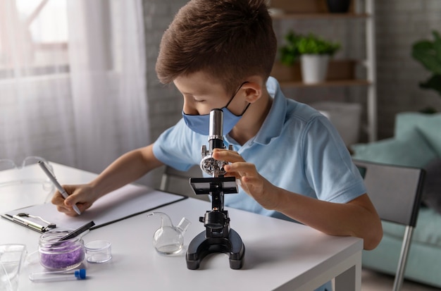 Niño de tiro medio aprendiendo con microscopio