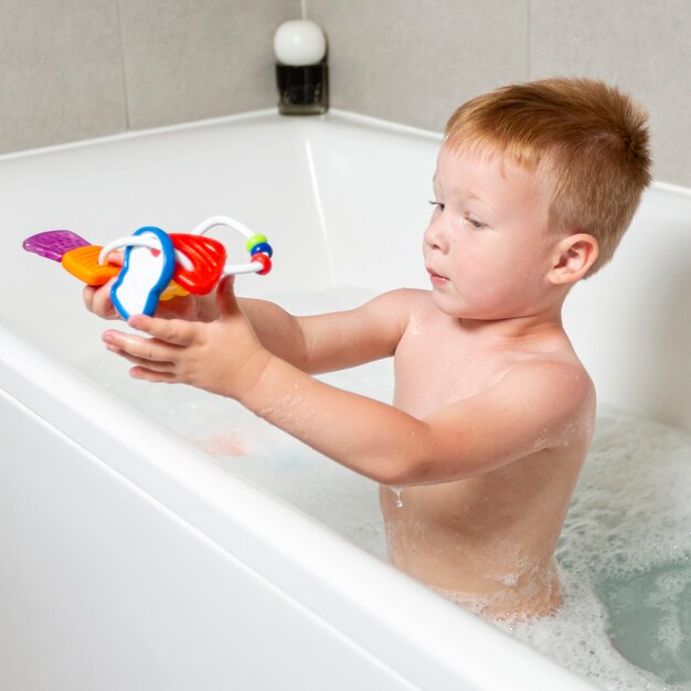 Niño de tiro medio con juguete en la bañera