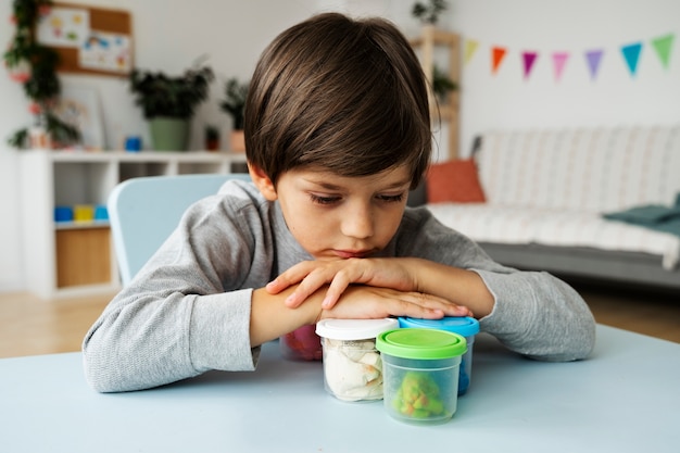 Foto gratuita niño de tiro medio con recipientes de plastilina.