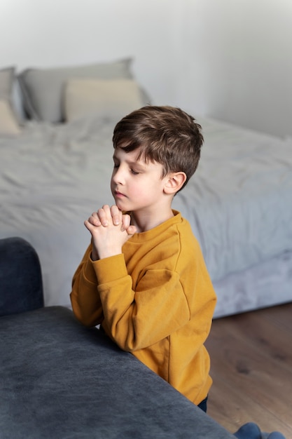 Niño de tiro medio rezando en el piso