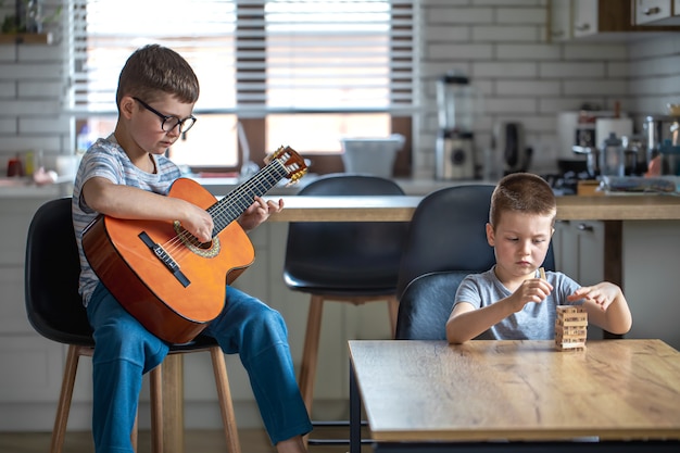 Un niño toca la guitarra y su hermano construye una torreta con cubos de madera en casa en la mesa.