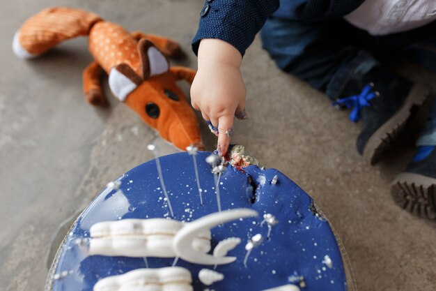 Niño tocando el pastel de cumpleaños con sus dedos. Concepto de fiesta del principito.