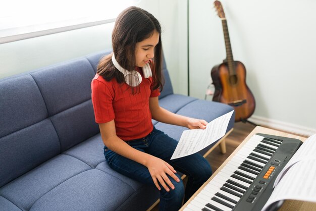 Niño tocando el teclado. Hermosa chica leyendo una partitura y aprendiendo a tocar el piano mientras practica sus lecciones de música en la sala de estar