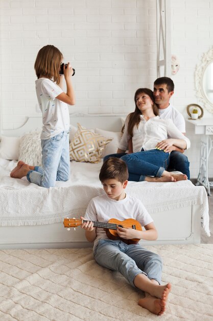 Niño tocando el ukelele frente a su hermana tomando fotos de sus padres