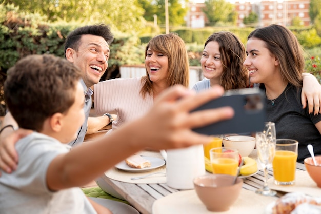 Foto gratuita niño tomando selfie de familia almorzando juntos al aire libre