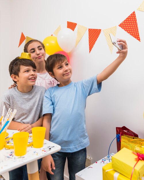 Niño tomando selfie con sus amigos en el teléfono móvil durante la celebración de cumpleaños